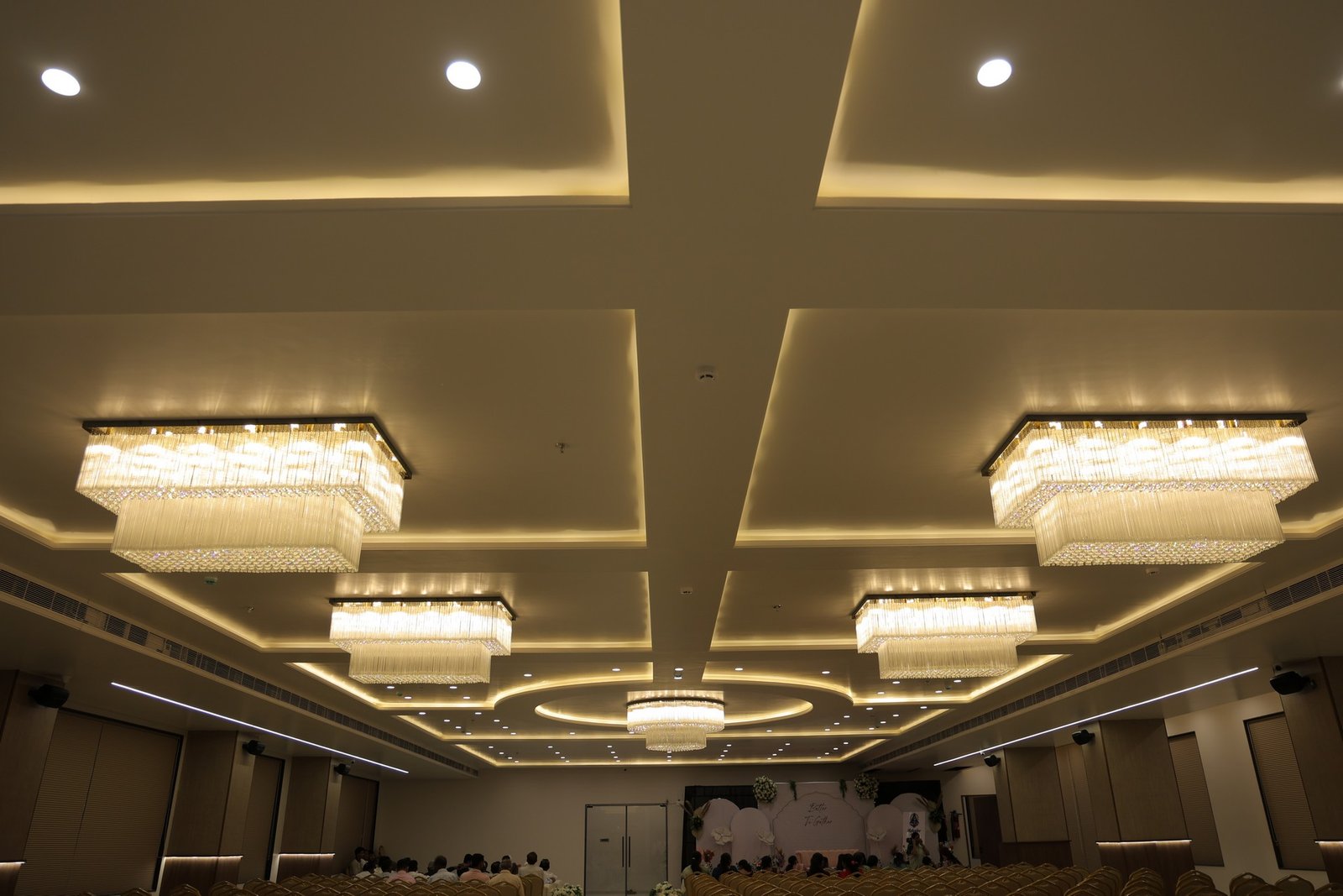 Elegant indoor lounge with pink velvet seating around a cherry blossom tree, a floral-decorated staircase, and a large chandelier overhead.